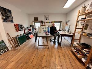 un homme assis à un bureau dans une pièce dans l'établissement Grande chambre chez l'artiste-peintre, à La Réole