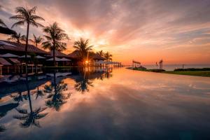 a sunset over a swimming pool with palm trees at The Anam Cam Ranh in Cam Ranh