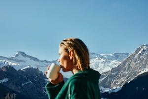 a woman drinking a cup of coffee in front of mountains at The Cambrian in Adelboden