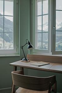 uma secretária com um candeeiro num quarto com janelas em The Cambrian em Adelboden