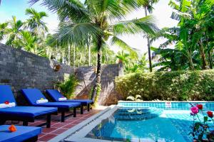 a resort pool with blue lounge chairs and palm trees at Rural Scene Villa in Hoi An