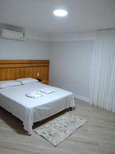 a bedroom with a white bed with a wooden headboard at Horto Executivo Hotel in Ipatinga