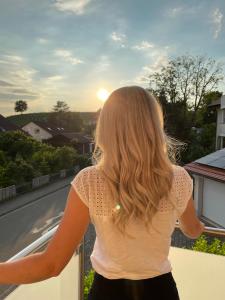 a woman standing on a balcony looking at the sunset at Seebrise mit Musik und Wein in Meersburg