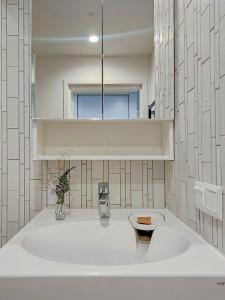 La salle de bains blanche est pourvue d'un lavabo et d'un miroir. dans l'établissement Comfy Rest apartamentai Kalno namuose, à Juodkrantė