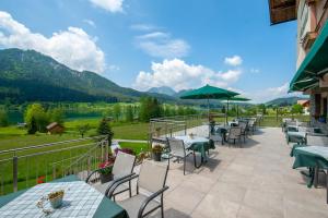 a patio with tables and chairs with mountains in the background at Wiesenhof, Hotel direkt am See in Weissensee