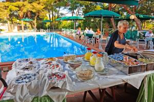a man standing at a table with food next to a pool at Hotel Kyrie Isole Tremiti in San Domino