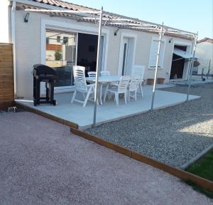 un patio con sillas blancas, una mesa y una parrilla en Maison individuelle neuve avec piscine en Limoux