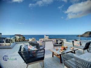 un patio con sillas, mesas y el océano en Pearls Beach Penthouse, en Porto Moniz