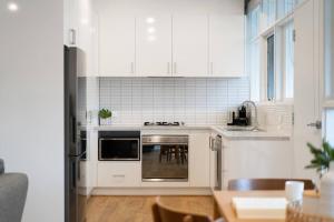 La cuisine est équipée de placards blancs et d'un four avec plaques de cuisson. dans l'établissement Modern Stylish Self-contained Apartment, à Burnside