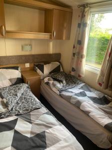 two beds in a small room with a window at Prestige Static Caravan on 5 Star Holiday Park in Cheswick