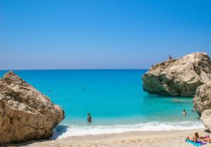 a beach with people in the water and large rocks at Seaview Kaposantes Apartments in Lefkada