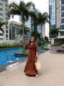a woman in a brown dress standing in front of a pool at Josh's Place at One Eastwood Avenue Tower 1 in Manila