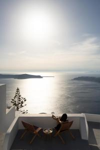 a person sitting on a balcony looking at the ocean at Serendipity Cliffside Villa & Suites in Imerovigli +55 photos