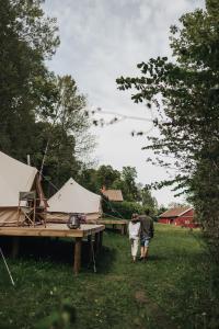 um homem e uma mulher a andar por um campo com tendas em Falkeröd - Lyxig glamping i naturreservat ink frukost em Grebbestad