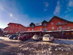 a large red building with cars parked in a parking lot at Hotel Lovac in Žabljak