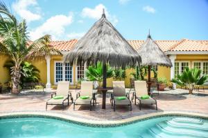 um resort com uma piscina e cadeiras e uma mesa com um guarda-sol de palha em Aruba Tropic Apartments em Noord