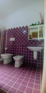 łazienka wyłożona fioletowymi kafelkami z 2 toaletami i umywalką w obiekcie Casa Vacanze VILLA SANDRINA w mieście Costa Paradiso