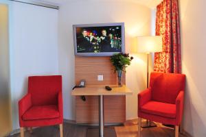Cette chambre dispose de 2 chaises rouges, d'une table et d'une télévision. dans l'établissement Hotel Aristella Swissflair, à Zermatt
