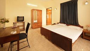 a hotel room with a bed and a desk and a television at KTDC Garden House in Palakkad