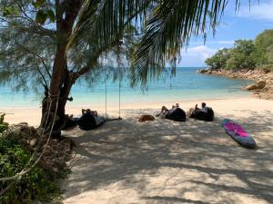 a group of people sitting on a beach next to the ocean at Coconut Beach Bungalows in Chaloklum