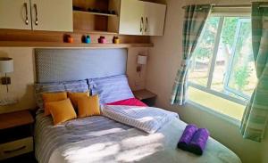 a bed with purple and yellow pillows and a window at Avonmore Martello Beach in Clacton-on-Sea
