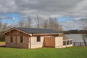 a small wooden shed with a black roof in a field at Waters Edge Retreat in Naseby