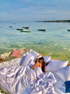 kobieta leżąca w łóżku pod poduszkami na plaży w obiekcie Indigo Blue Ceningan w mieście Nusa Lembongan