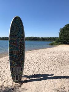 a surfboard standing on a sandy beach next to the water at DW_Bungalow am schönen Badesee Grünewalder Lauch in Lauchhammer