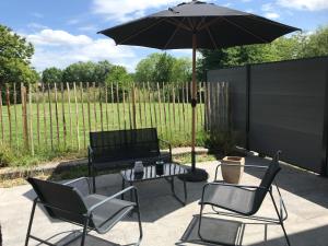 un patio con mesa, sillas y sombrilla en La grange de thoricourt en Thoricourt