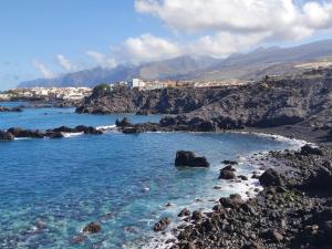 einen Strand mit blauem Wasser, Felsen und Bergen in der Unterkunft Apartamento HAKUNA MATATA con gran terraza, planta baja in Playa de San Juan