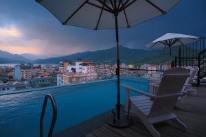 a swimming pool with a chair and an umbrella at Aabas Pokhara by Barahi Hospitality in Pokhara