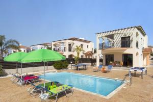 a swimming pool with chairs and umbrellas next to a house at Villa Kassiopeia by Villa Plus in Peyia