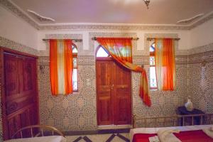 een slaapkamer met 2 ramen met oranje gordijnen en een bed bij Riad Haddaji Fes in Fès