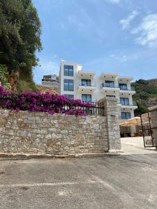 a stone wall with purple flowers in front of a building at Hotel Platon in Sarandë