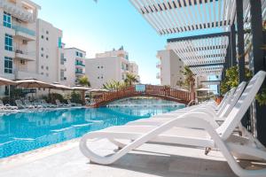 a pool with white lounge chairs and a bridge at Ledina Hotel in Orikum