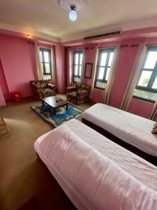 two beds in a room with pink walls and windows at The Nest Guest House in Changunarayan