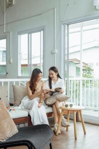 Duas mulheres sentadas num sofá a ler um livro. em Connect Hostel em Chiang Rai
