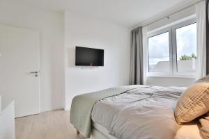 a white bedroom with a bed and a tv on the wall at Ostsee Suite 3 - Strandperle in Niendorf