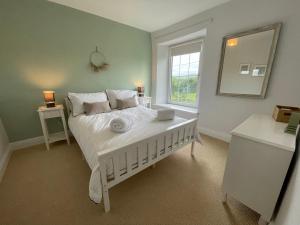 a bedroom with a white bed with a mirror and a window at Cosy country cottage with log fireplace and views in Kendal