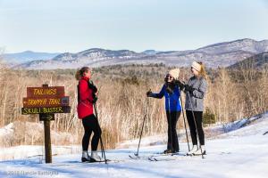 Tre donne sugli sci in piedi accanto a un cartello di Garnet Hill Lodge a North River