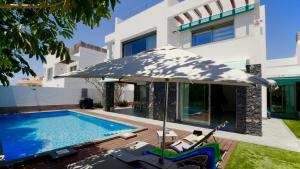 a pool with an umbrella and chairs next to a house at Villa BLUE PORTOFINO Los Cristianos, POOL in Los Cristianos