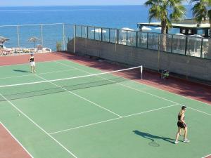 two women playing tennis on a tennis court near the ocean at Avra Beach Resort in Ixia