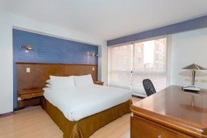 1 dormitorio con cama blanca, escritorio y ventana en GIO Suites Parque 93 Bogotá, en Bogotá