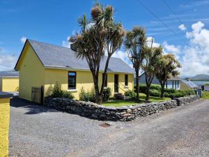 a yellow house with palm trees next to a street at Kate's Cottage in Valentia Island