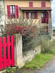 a red fence in front of a house with flowers at Maison de campagne chaleureuse et au calme in Léotoing
