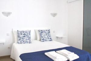 a white bedroom with a bed with blue and white pillows at Sudoeste Guest House in Odeceixe
