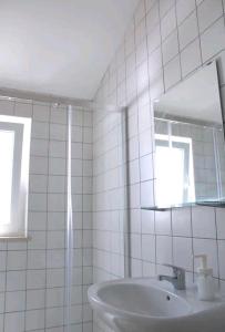 a white tiled bathroom with a sink and a mirror at Sudoeste Guest House in Odeceixe
