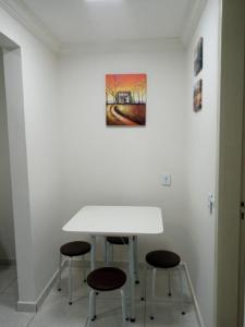 a white table with three chairs and a painting on the wall at Espaço completo bem localizado c estacionamento in Foz do Iguaçu