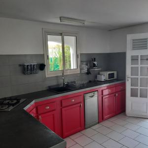 a kitchen with red cabinets and a sink and a window at Spacieux cocon in Goyave