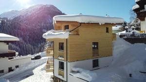 a building covered in snow with a mountain in the background at ARLhome - Zuhause am Arlberg in Sankt Anton am Arlberg